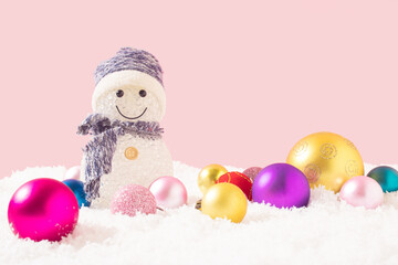 Snowman and brilliant party decorations in the snow. Pastel pink background. Minimal winter, Christmas, New Year,  holiday concept. Frontal view. Copy space.