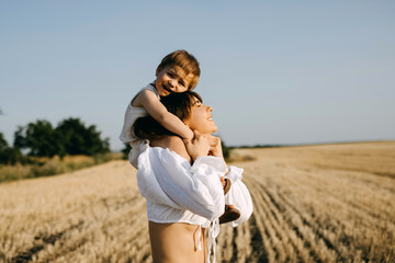 Mother playing with her daughter, holding her up on shoulders, outdoors, laughing.