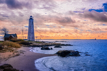 New Haven Landmark Lighthouse at the beachfront of Morgan Point Park, built in 1847 in Connecticut. Winter coastal landscape of New England with dramatic clouds, and glacial rocks. - obrazy, fototapety, plakaty