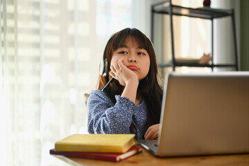 Tired and bored schoolgirl studying online on laptop at home. Online education concept.