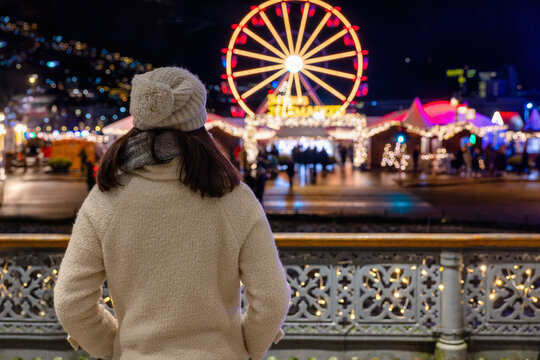 A tourist woman stands in front of the illuminated Christmas market of Bergen, Norway, during winter night