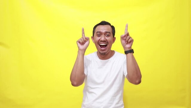 Hands, pointing and up with a man on a yellow screen background in studio to promote product mockup. Hand gesture, happy and smile with a adult male showing empty chromakey space above her head
