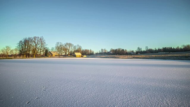 Frozen lake by a farmhouse in winter - time lapse with shadows crossing the snow