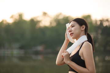 Young Asian woman takes a relaxing walk, wiping off sweat after jogging in the park.