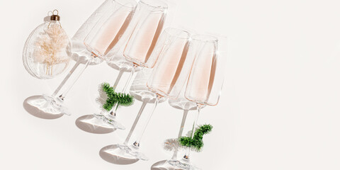 Minimal trend New Year party concept, flat lay of rose wine in champagne glasses, Christmas green tinsel and ball as  xmas decor. Holiday banner, top view wineglass at sunlight, sun glare