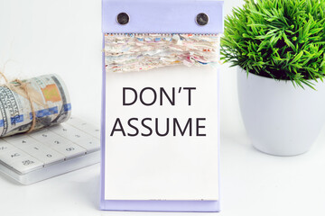 DON'T ASSUME text, word, inscription on a desktop calendar on a white background next to money and a green flower