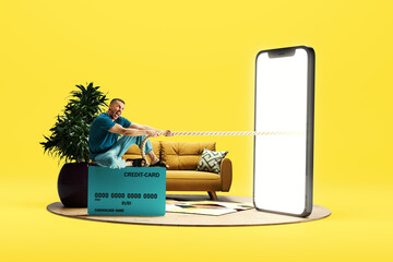 Emotional man sitting on credit card and pulling robe from giant 3D model of mobile phone with empty screen over light background. Online shopping, sales, e-payment - obrazy, fototapety, plakaty