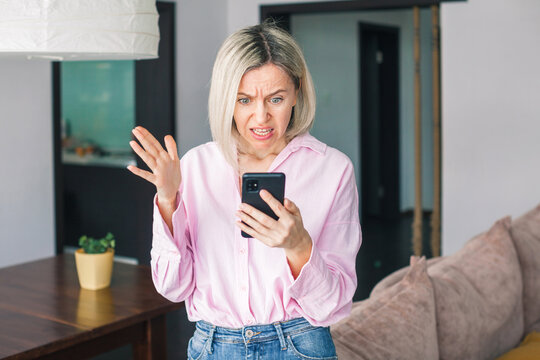 middle-aged woman holding phone, reading unpleasant news in social media