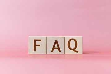 FAQ text on wooden cubes on a pink background, close-up
