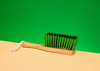 An eco friendly wooden brush with green bristles rests on a green background. Household cleaning.