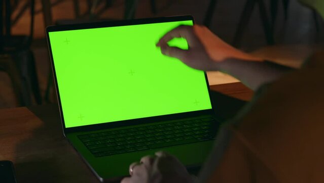A hacker or Internet computer scammer opens his laptop in a dark room and starts typing on the keyboard. A green screen on the display for overlaying graphics or media. High quality 4k footage