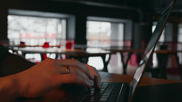 A close-up of the hands of a hacker or Internet fraudster who is typing text or texting in a messenger using the keyboard of his laptop in a dark room of an empty cafe. High quality 4k footage