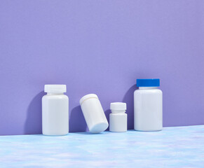 White jars with pills of different sizes on the table. Treatments for various diseases. Copy space for text. Tablets, pills and dietary supplements. - obrazy, fototapety, plakaty