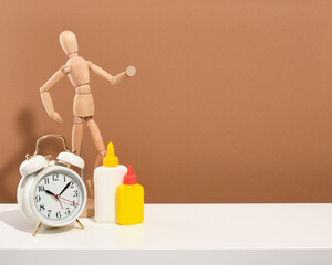 A wooden man, a white old vintage alarm clock and stationery glue on a white table. Copy space for...
