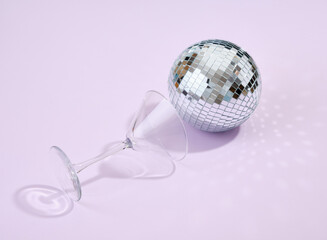 Empty alcohol beverage glass and glowing bright disco ball on a purple background. Night funny relax.