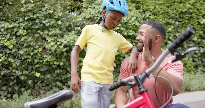 Happy african american father and son with bicycle high fiving in garden, slow motion