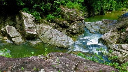Naklejka na ściany i meble Mountain river in the jungle. The flow of a mountain river moves over the stones, forming a cascading waterfall, among the humid tropical forest.
