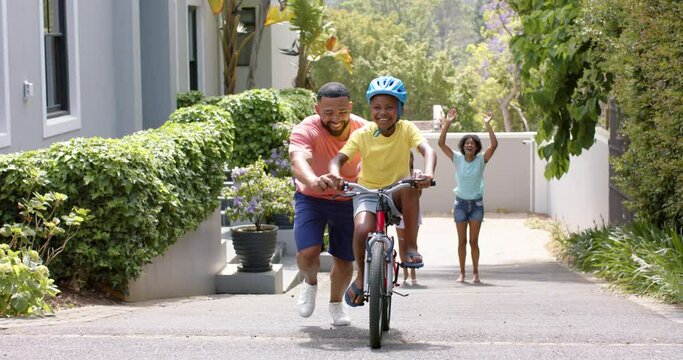 African american father teaching son to ride bicycle, mother and sister cheering, slow motion