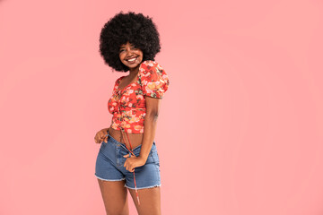 African american fashionable female in trendy jeans shorts posing over pastel pink studio...
