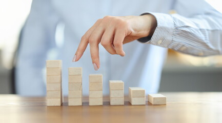 Woman stepping her fingers on graphic made of wooden cubes closeup. Career growth concept