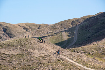A group of comrades helps a fallen motorcyclist. A motorcyclist rides on a wheelie. Mountain, cross-country motorcycle on the rear wheel. Extreme sports in the desert.