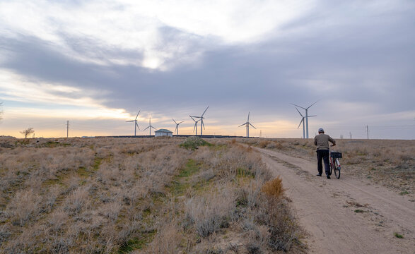 A man with a bicycle walks along a country road towards installed wind generators. A man with a bicycle against the backdrop of an ecological power plant.