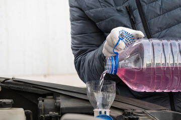 A man pours glass washer fluid into the tank of a car.