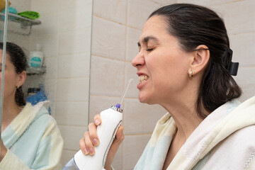 A 40-year-old woman brushes her teeth with an irrigator. A woman looks in the bathroom mirror and...