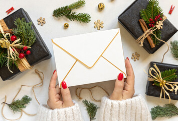 Hands with Blank envelope near Christmas decor, gift boxes and fir branches, mockup
