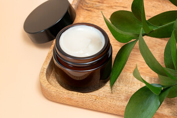 close up of collagen cream in glass jar and green leaves on beige background. skin and body care beauty products. Mockup