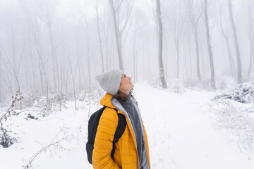 Fototapeta na wymiar Happy caucasian woman in yellow jacket enjoying walking and snowfall in winter forest, exposing her face to snowflakes