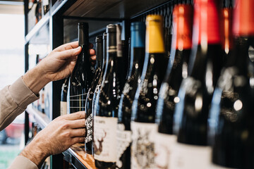 Customer Selecting Wine Bottle from Store Shelf. A person's hand picking a wine bottle from a diverse selection on a well-stocked wine shop shelf