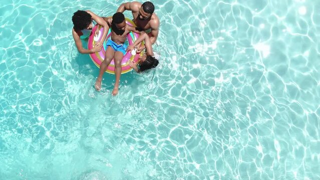 Aerial of african american parents, son and daughter playing on inflatable in sunny pool, copy space