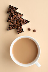 Coffee with milk in a white cup and a christmas tree made of coffee beans on a beige background. Christmas and New Year concept. Top view