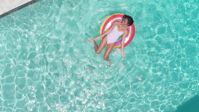 Aerial of happy african american teenage girl playing on inflatable in sunny pool, copy space