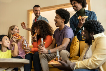 Group of multiethnic friends on a couch eating pizza and drinking beer at a house party, while laughing telling stories - obrazy, fototapety, plakaty
