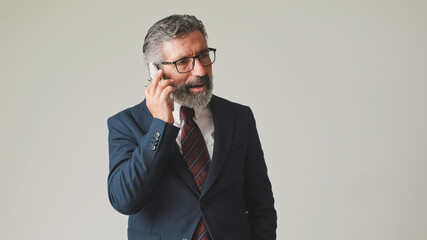 Businessman in glasses with gray hair, talking on mobile phone, isolated on gray background in the studio