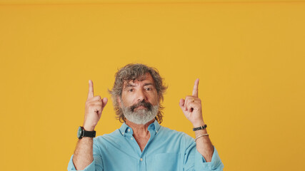 Elderly grey-haired bearded man wears blue shirt looking up points fingers up at at the copy space...
