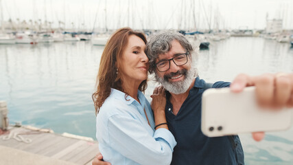 Happy elderly couple smiling confidently take selfie on mobile phone while standing in marina on...