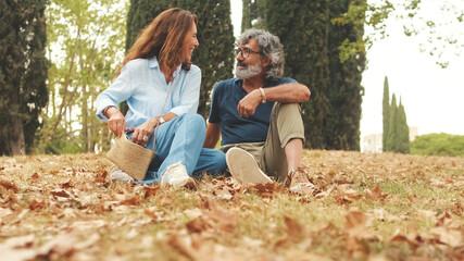 Retired couple talking, sitting on the grass in the park in autumn
