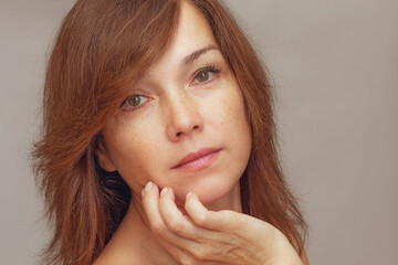 Portrait of cropped caucasian middle aged woman face with freckles holding fingers on cheek skin on...