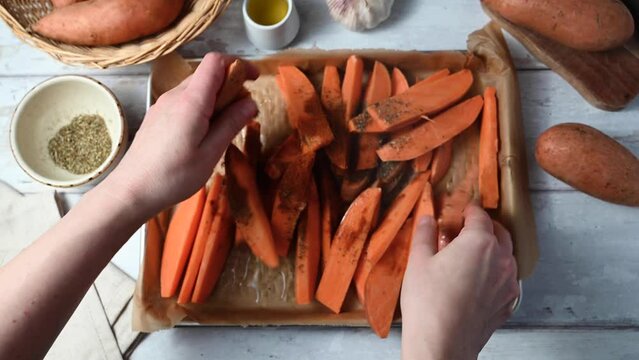 Cooking homemade sweet potato wedges, fries on a plate. Female hands mixing sliced potatoes with spices.