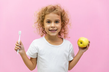 Portrait of cute curly hair little girl with open wide smile holding green apple and toothbrush...