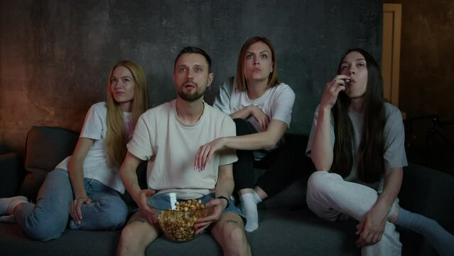 A group of four friends gathered to watch a movie at home. People watch a blockbuster on TV