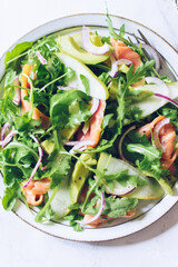 Healthy salad with arugula, smoked salmon, pear, avocado and red onion