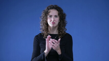 Woman clapping hands congratulating viewer standing on blue background looking at camera signalling approval with thumbs up