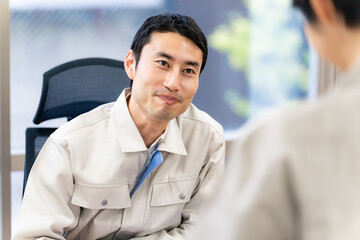 オフィスで部下と会話する作業服の男性