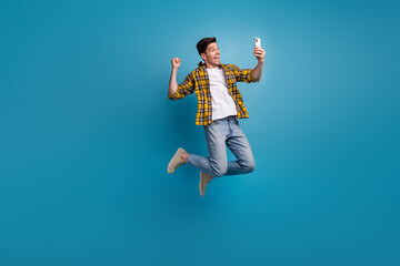 Full size body photo of funny man in air jumping with smartphone makes selfie shows his emotions...