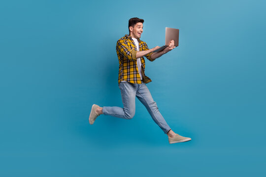 Full body length photo addicted programmer loves doing his job in deadline running jumping with computer isolated on blue color background