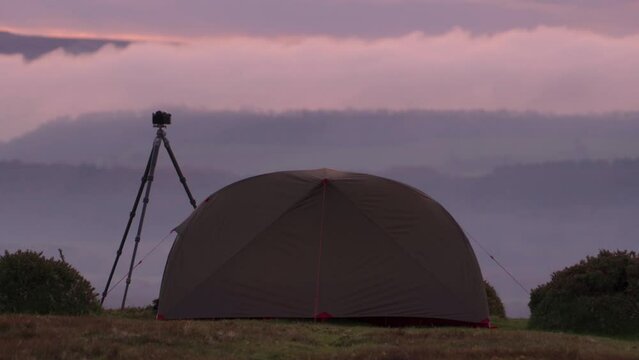 A wild camping tent and camera tripod on a mountain summit in gorgeous morning cloud
